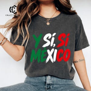 Può includere: Una t-shirt grigio antracite a maniche corte con la scritta Y SÍ, SÍ MÉXICO stampata in stile pennellata. Le lettere sono colorate in verde, bianco e rosso, richiamando i colori della bandiera messicana. La t-shirt ha un girocollo.