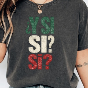 Può includere: Una t-shirt a maniche corte grigio antracite con una stampa grafica dall'aspetto vissuto che riporta il testo ¿Y SI? SI? SI? in righe sovrapposte. La riga superiore è verde, quella centrale è bianca e quella inferiore è rossa.