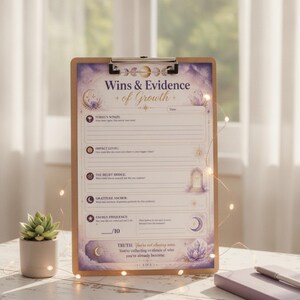 May include: A wooden clipboard holding a printed sheet titled Wins & Evidence of Growth. The paper features purple celestial graphics, moon phases, and sections for daily reflections including impact level, belief bridge, gratitude anchor, and energy frequency.