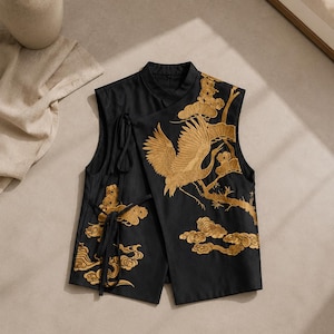Peut inclure: Un gilet noir sans manches orné de broderies dorées représentant une grue, des branches de pin et des nuages stylisés. Le vêtement possède un col officier, une fermeture frontale asymétrique et des liens en tissu noir sur le côté.