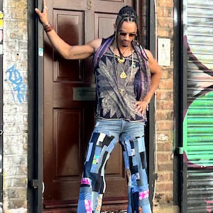 May include: A sleeveless black tank top with a large, light-colored feather graphic print, paired with wide-leg jeans featuring a patchwork design of various blue denim shades, black fabric panels, and small colorful patterned fabric accents.