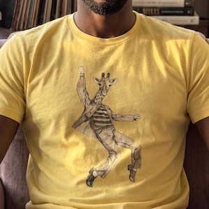 May include: A bright yellow short-sleeved t-shirt featuring a black and white line art illustration of a giraffe standing on its hind legs, wearing a striped shirt, a jacket, and trousers, captured in a dynamic pose with one arm raised high.