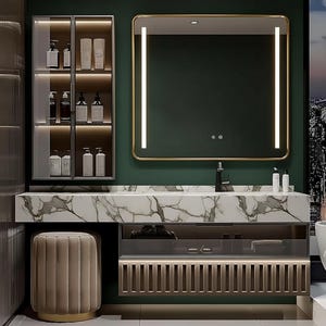 May include: A bathroom vanity set featuring a white marble countertop with grey veining, a rectangular mirror with integrated vertical LED lights and a gold frame, a wall-mounted glass cabinet with internal lighting, and a beige tufted cylindrical stool.