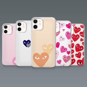 May include: Five phone cases with heart designs. The cases are in various colors, including pink, white, and peach. The heart designs feature eyes, and the cases are made of clear plastic.
