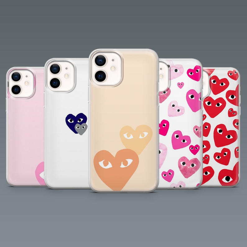 May include: Five phone cases with heart designs. The cases are in various colors, including pink, white, and peach. The heart designs feature eyes, and the cases are made of clear plastic.