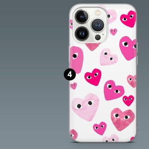 May include: White iPhone case with a repeating pattern of pink hearts with black eyes. The hearts vary in size and shade, creating a playful design. The case has a clear border and a camera cutout.