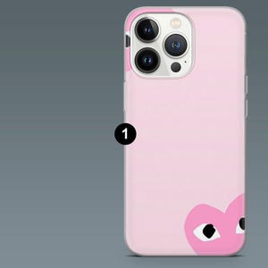 May include: A pink phone case featuring a graphic of a heart with eyes. The case has a smooth finish and a camera cutout. The phone case is designed to fit a smartphone.