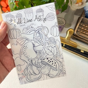 May include: A clear plastic package containing black and white die-cut stickers featuring autumn-themed illustrations of mushrooms, pumpkins, acorns, and leaves. The backing card displays the text Fall Line Art DIECUTS with matching line art.