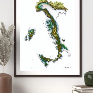 Peut inclure: Une impression d'art encadrée représentant une carte en relief tridimensionnelle de l'Italie. La carte affiche un terrain varié dans des tons de vert, brun et blanc sur un fond blanc. Le mot ITALY est imprimé en noir dans le coin inférieur droit.