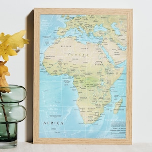 Peut inclure: Une carte murale encadrée du continent africain présentant une masse terrestre beige clair sur un fond d'océan bleu. La carte inclut les noms des pays, les grandes villes et le texte AFRICA en bas à gauche avec une échelle de 1:51 400 000.