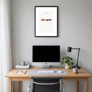 Puede incluir: Una lámina de arte enmarcada que presenta el texto QWERTY sobre una fila horizontal de cinco pequeños cuadrados de colores rojo, amarillo, azul, negro y azul, sobre un fondo crema dentro de un marco negro fino colgado en una pared gris claro.