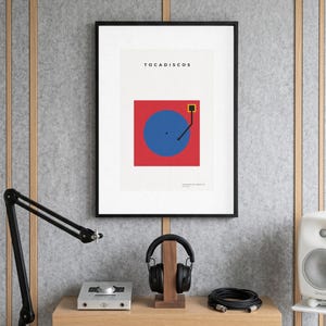 Puede incluir: Una lámina de arte mural enmarcada que presenta una ilustración gráfica de un tocadiscos con un plato circular azul sobre un fondo cuadrado rojo. El texto TOCADISCOS está impreso en negro en la parte superior, con texto más pequeño abajo.
