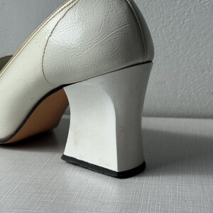 K&ouml;nnte beinhalten: Wei&szlig;e Lederschuhe mit Absatz und quadratischem Blockabsatz. Der Absatz ist wei&szlig; mit einem schwarzen Rand an der Unterseite.