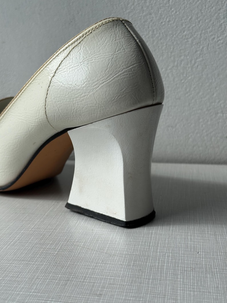 K&ouml;nnte beinhalten: Wei&szlig;e Lederschuhe mit Absatz und quadratischem Blockabsatz. Der Absatz ist wei&szlig; mit einem schwarzen Rand an der Unterseite.