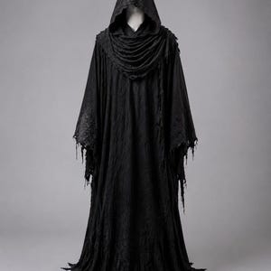 May include: A floor-length black hooded robe featuring a draped cowl neckline and long, wide sleeves with distressed, frayed edges. The fabric has a textured, weathered appearance, extending into a jagged, uneven hemline at the bottom.