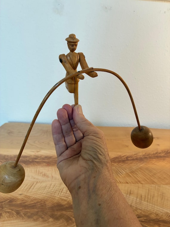 A hand-carved Japanese yajirobe balancing toy — a centuries-old kinetic folk art form where a little gondolier man defies gravity on a fingertip, no batteries needed.