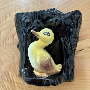 May include: A glossy black ceramic planter shaped like a tree stump with a three-dimensional yellow duck figurine attached to the front. The duck has brown accents on its wings and beak, and the black stump features a textured, bark-like surface.
