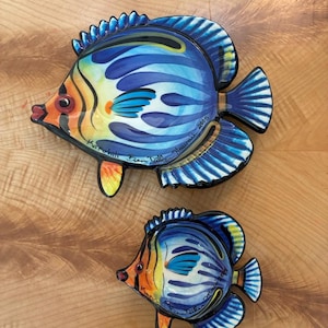 Puede incluir: Dos platos de cerámica pintados a mano con forma de pez en diferentes tamaños, con patrones vibrantes en azul, naranja, amarillo y negro. Cada plato muestra el texto Kapalua Ben Diller Hawaii 2005, con diseños detallados de aletas y escamas.