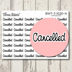May include: A sticker sheet featuring multiple rows of the word Cancelled printed in a black cursive font. The top right corner displays the text Three Sisters and BWT-7-1030-N CANCELLED. A large pink circle overlays the center with the word Cancelled.