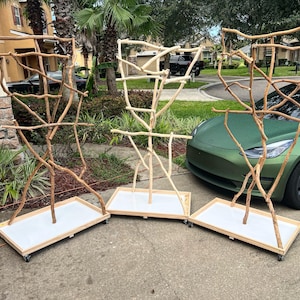 May include: Three wooden bird perches with natural branch structures. Each perch has a rectangular white tray base with wheels. The perches are various shades of brown and tan, and are designed for pet birds.