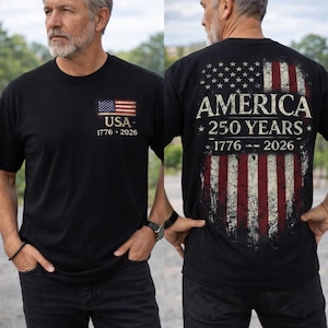 May include: A black short-sleeved t-shirt featuring a small American flag graphic on the front chest with the text USA 1776-2026. The back displays a large, distressed American flag graphic with the text AMERICA 250 YEARS 1776-2026.