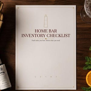 Könnte beinhalten: Eine weiße Checkliste für die Hausbar mit dunkelrotem Text HOME BAR INVENTORY CHECKLIST und Track what you have. Know what you need. Umgeben von einem goldenen Cocktailshaker, einem Messbecher, einem Glas und verschiedenen Zitrusfrüchten.
