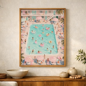 Op de afbeelding: Een ingelijste kunstdruk toont een levendige zwembadscène met zwemmende en zonnebadende mensen. Het kunstwerk toont een turquoise zwembad, roze parasols en een retro motel. De print zit in een houten lijst.