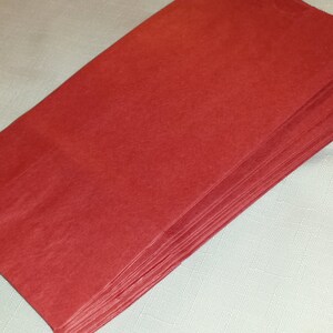 Puede incluir: Una pila de hojas de papel de seda rojas. Las hojas son rectangulares y tienen una superficie ligeramente texturizada. El papel es de un color rojo s&oacute;lido y vibrante. La pila est&aacute; cuidadosamente dispuesta, con los bordes alineados.