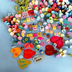 May include: Assortment of colorful, decorative, wooden, and metal charms with various words and designs. The charms include words like "love", "grow", "believe", "hope", "dream", "spring", "friendship", and "petal patch".