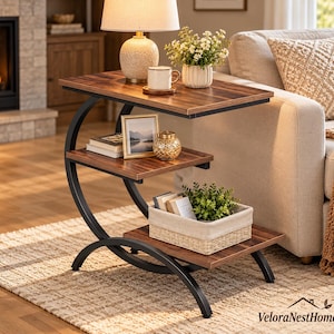 May include: A three-tier side table with a dark wood grain finish and a curved black metal frame. The table features a rectangular top, a middle shelf, and a bottom shelf, providing storage for books, a picture frame, and a woven basket.