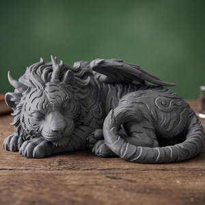 May include: A gray fantasy creature figurine with a lion-like face, horns, and wings, resting on a wooden surface. The sculpture has intricate details and a curled tail. A leather-bound book, inkwell, and quill are in the background.