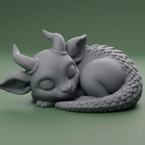Puede incluir: Una figura de dragón gris durmiente con cola enroscada, cuernos y orejas grandes. El dragón está tumbado con los ojos cerrados, lo que le da un aspecto tranquilo. La figura está sobre un fondo verde liso.