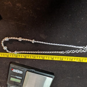 May include: A silver bracelet with a twisted rope design and sparkling accents. The bracelet is measured with a yellow tape measure. The bracelet is approximately 7 inches long.