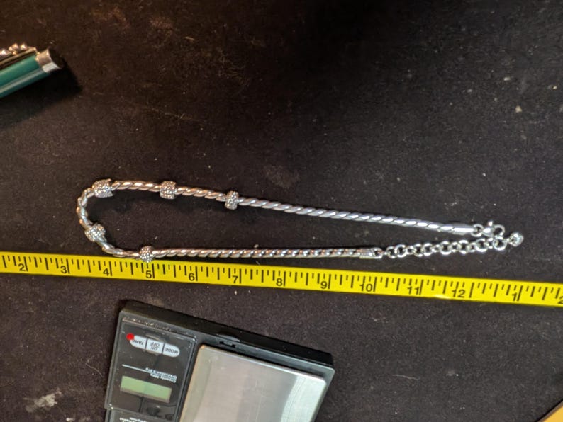 May include: A silver bracelet with a twisted rope design and sparkling accents. The bracelet is measured with a yellow tape measure. The bracelet is approximately 7 inches long.