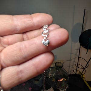 May include: A silver-colored chain bracelet with a heart-shaped charm. The charm is suspended from a series of linked heart-shaped links. The bracelet is held in a person's hand.