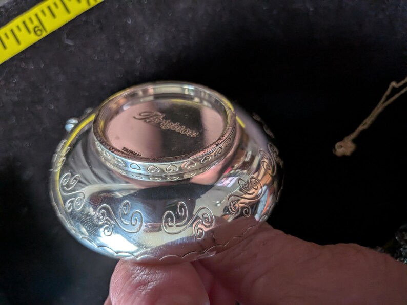 May include: A silver-toned metal bowl with a polished finish and engraved swirl patterns along the exterior. The base features the embossed text Brighton and TAIWAN. A yellow measuring tape is visible in the corner showing a 15.24 cm mark.