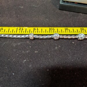 May include: A silver-colored bracelet with three clear, round, decorative beads. The bracelet is measured with a yellow ruler. The beads are approximately 0.25 inches in diameter.