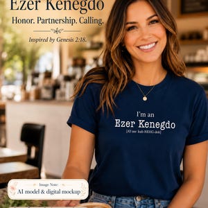 May include: A navy blue t-shirt featuring the white text I'm an Ezer Kenegdo [AY-zer kuh-NEHG-doh]. The shirt has short sleeves and a crew neckline. The text is printed in a clear, sans-serif font centered on the chest area of the garment.