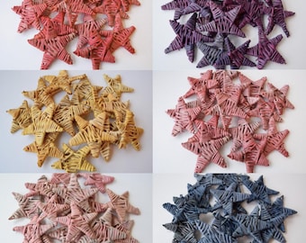 May include: A collection of six groups of star-shaped ornaments, each crafted from coiled material. The sets feature distinct color palettes including shades of coral, deep purple, golden yellow, dusty rose, light pink, and slate blue.