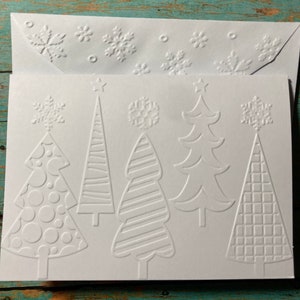May include: White Christmas greeting card with embossed designs of Christmas trees and snowflakes. The card has a matching envelope with embossed snowflakes. The trees have different patterns and shapes.