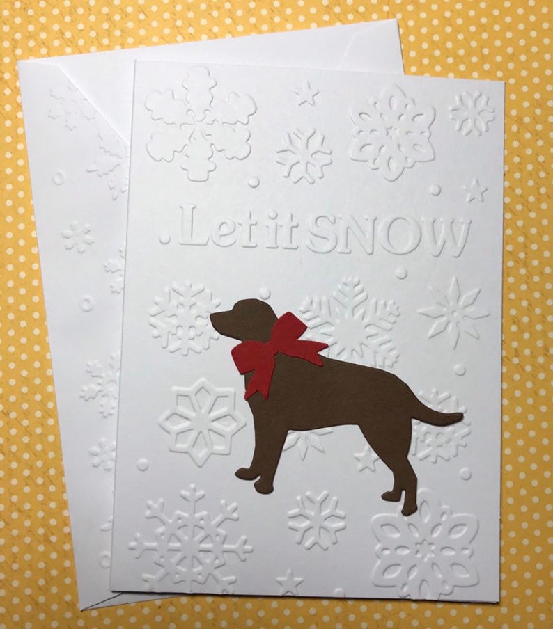 May include: White greeting card with embossed snowflakes and the phrase "Let it SNOW." A brown dog silhouette with a red bow is featured. Includes a matching envelope.