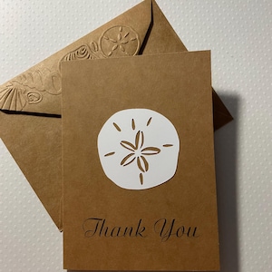May include: A brown card with a white cutout of a sand dollar and the text "Thank You" in black script.