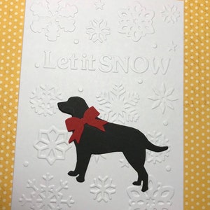 May include: White greeting card with embossed snowflakes and the phrase "Let it SNOW." A black silhouette of a dog with a red bow is featured on the card. The background is a yellow polka dot pattern.