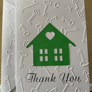May include: A white card with a green house cutout and the words "Thank You" in black script. The background is embossed with a pattern of keys.
