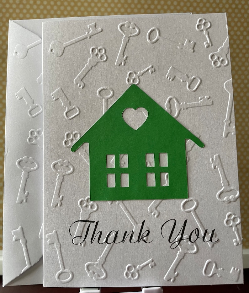 May include: A white card with a green house cutout and the words "Thank You" in black script. The background is embossed with a pattern of keys.