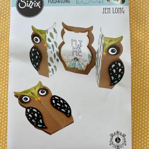 May include: A Sizzix Thinlits Fold-A-Long die set featuring owl designs. The set includes various owl shapes with decorative details, including the text "FLY WITH ME". The packaging also lists the number of dies included.