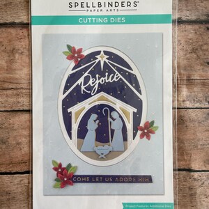 May include: A package of Spellbinders paper arts cutting dies. The design features a nativity scene with the word "Rejoice" and the phrase "Come let us adore him". The package includes 8 cutting dies.