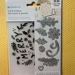 May include: A package of Moment cut and emboss paper crafting templates. The package includes an embossing folder with the words "MERRY AND" and various die-cut shapes, including leaves, snowflakes, and a heart. The package is on a yellow polka dot background.