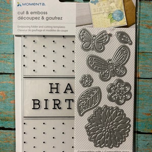 May include: A silver die-cutting set with eight pieces, including two butterflies, a flower, two leaves, and a "Happy Birthday" sentiment. The set is compatible with Sizzix, CuttleBug, and Spellbinders die-cutting machines. The packaging is white with black text and a silver background.