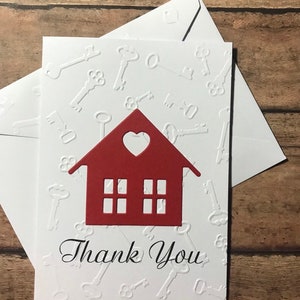 May include: A white card with a red house cutout and the words "Thank You" in black script. The background of the card is embossed with a pattern of keys.